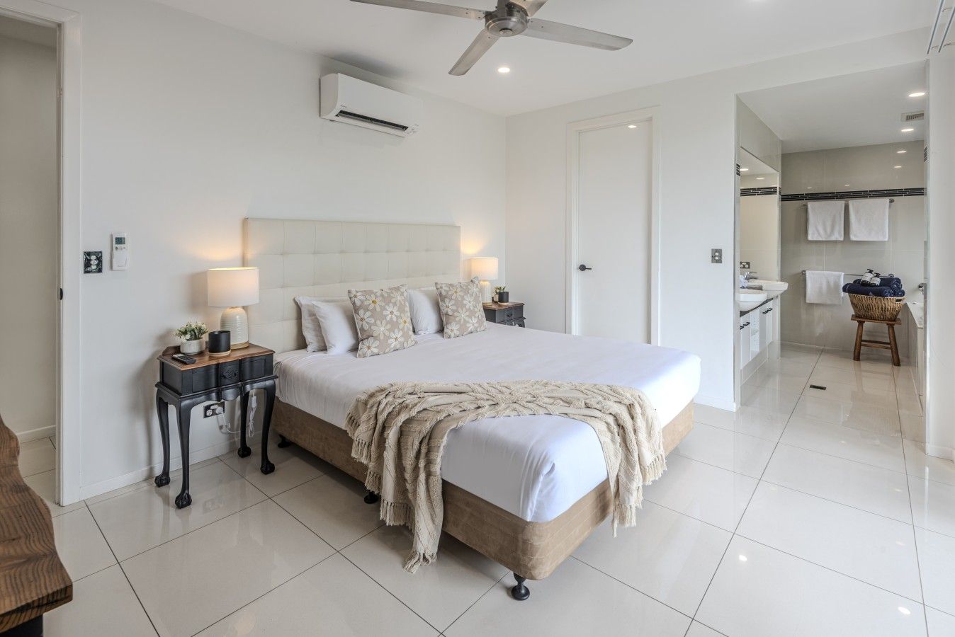 Een moderne slaapkamer met een groot bed, nachtkastjes, een plafondventilator en een badkamer die door een open deur zichtbaar is.