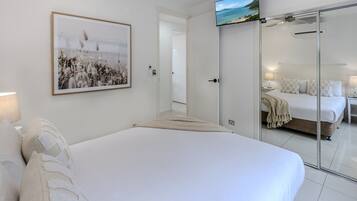 A modern bedroom with a large bed, a flat-screen TV, a framed picture, and a sliding door leading to another room.