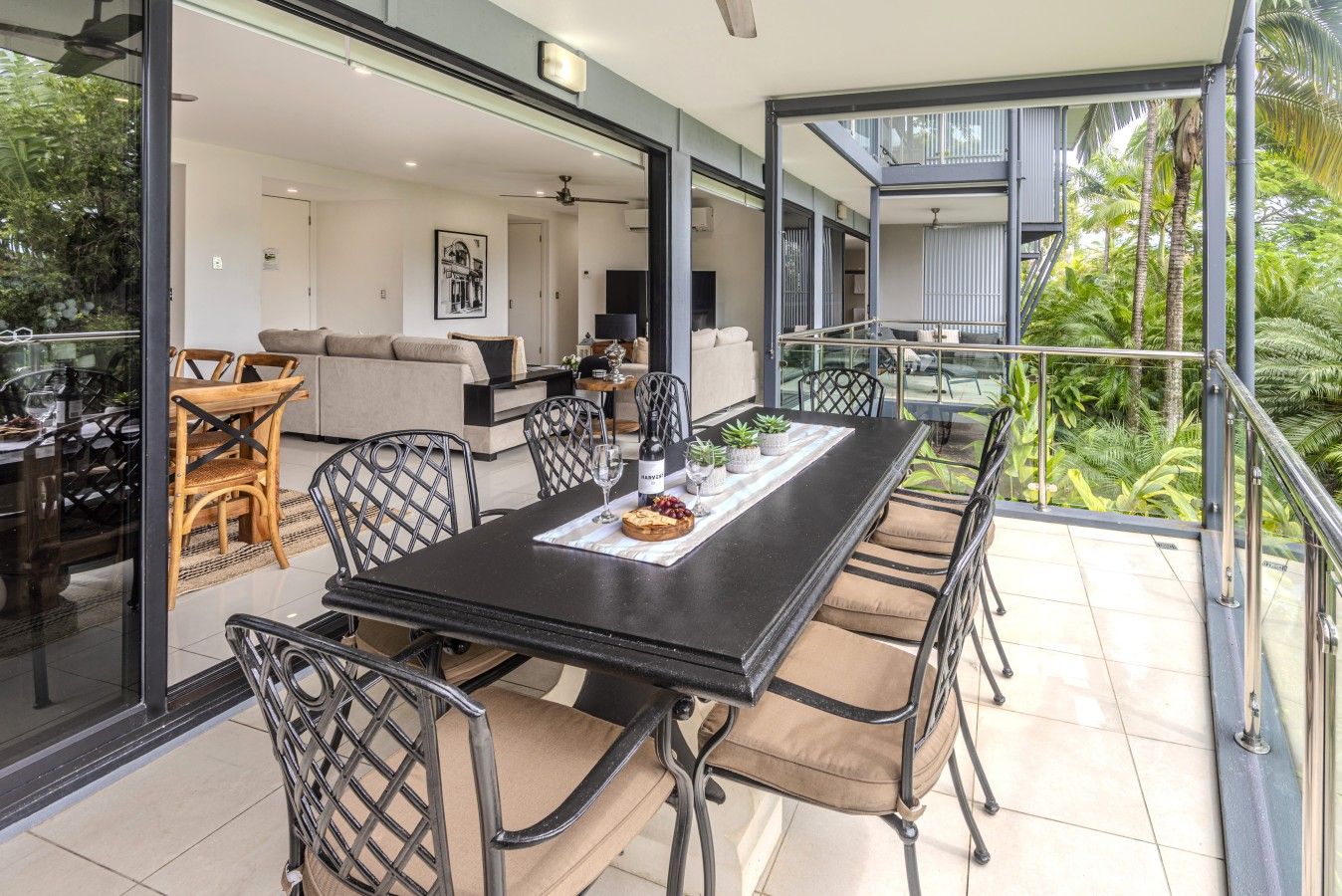 A modern dining area with a black table, beige cushioned chairs, and a glass balustrade overlooking a lush garden.