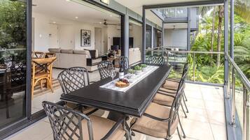 A modern dining area with a black table, beige cushioned chairs, and a glass balustrade overlooking a lush garden.