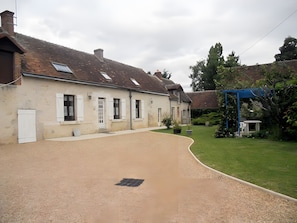 A residential building with a gravel driveway, a blue pergola, and a well-maintained lawn.