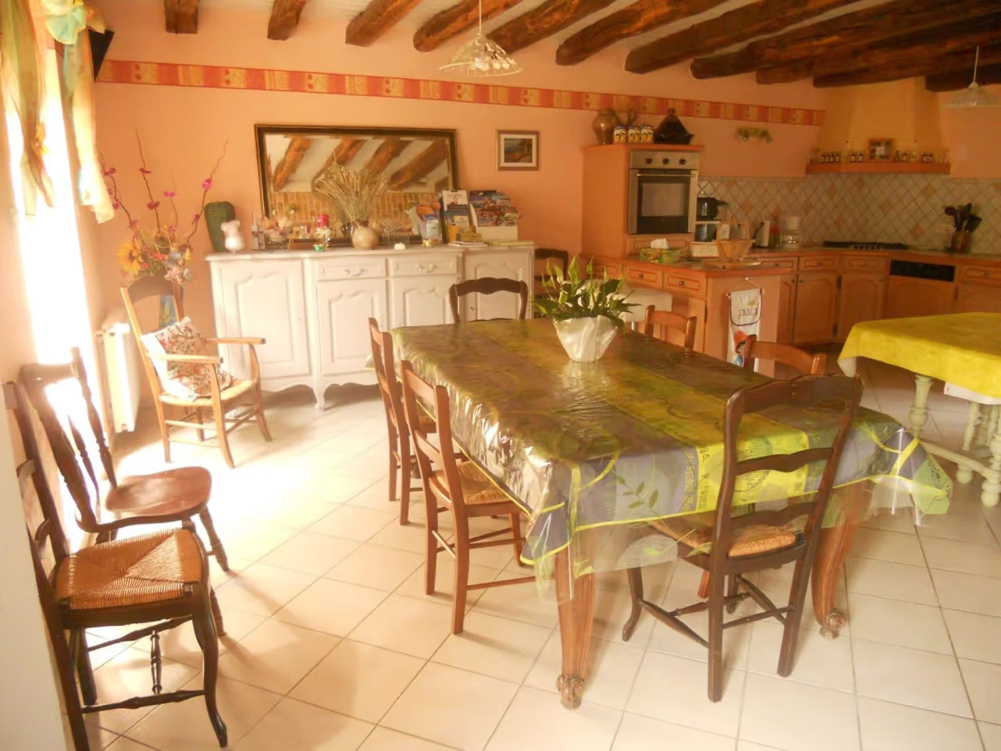 Un comedor con una mesa cubierta con un protector, sillas de madera y una cocina al fondo.