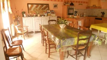 Un comedor con una mesa cubierta con un protector, sillas de madera y una cocina al fondo.