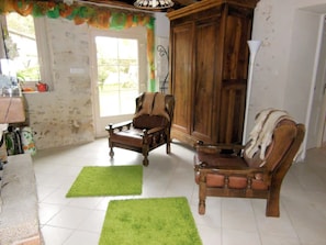 Una sala de estar con dos sillones de madera, un tapete verde, un aparador de madera y un ventanal con vistas.