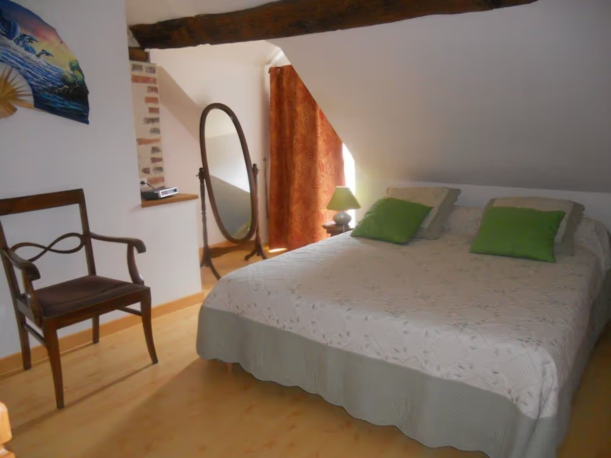 Une chambre à coucher avec un lit, une chaise, un miroir et une fenêtre avec des rideaux.
