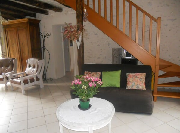 A living room with a wooden staircase, a sofa with pillows, a chair, and a table with a potted plant.