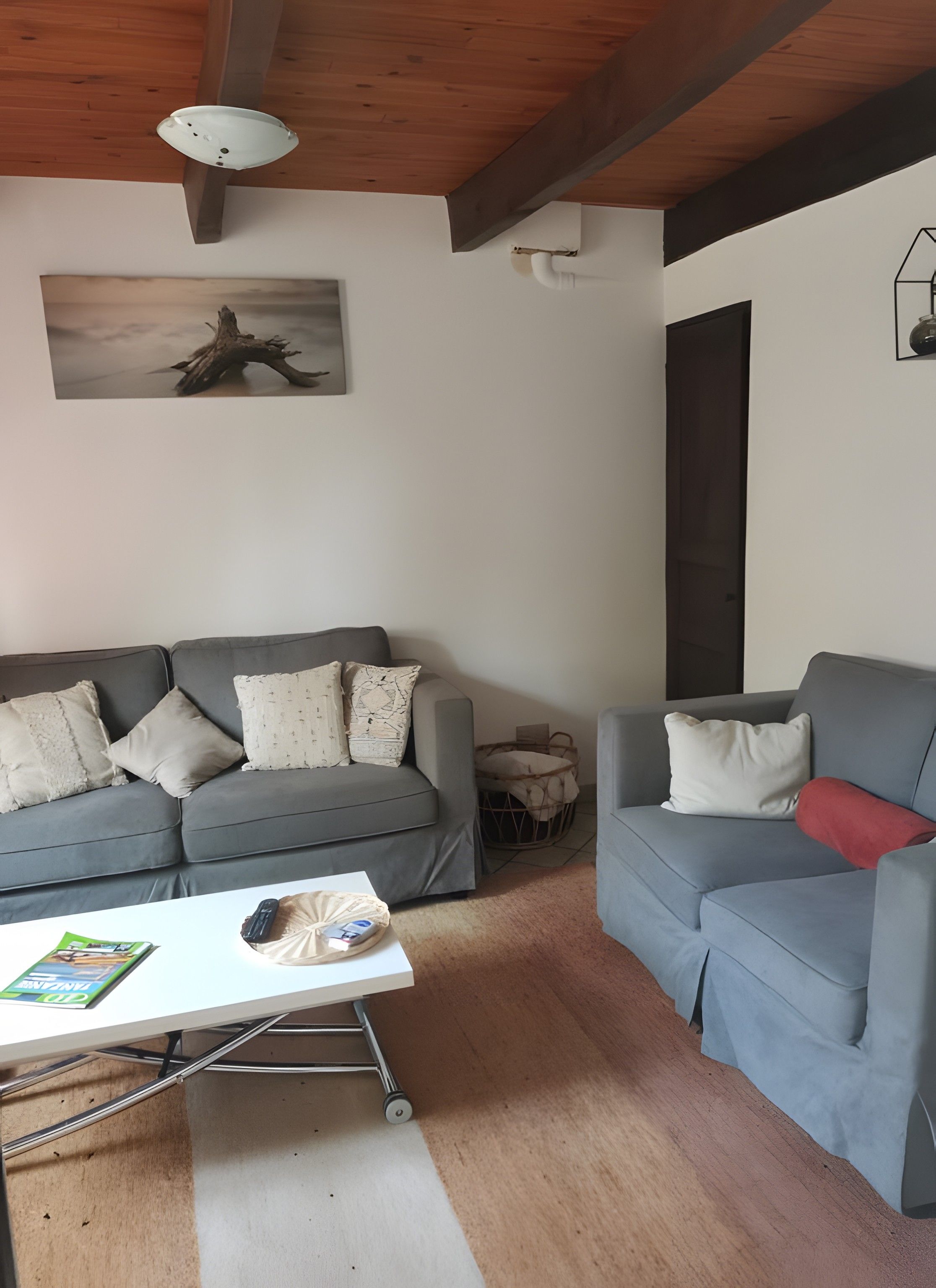 Ein Wohnzimmer mit zwei grauen Sofas, einem Couchtisch, einem Wandbild und einer Holzzahlende.