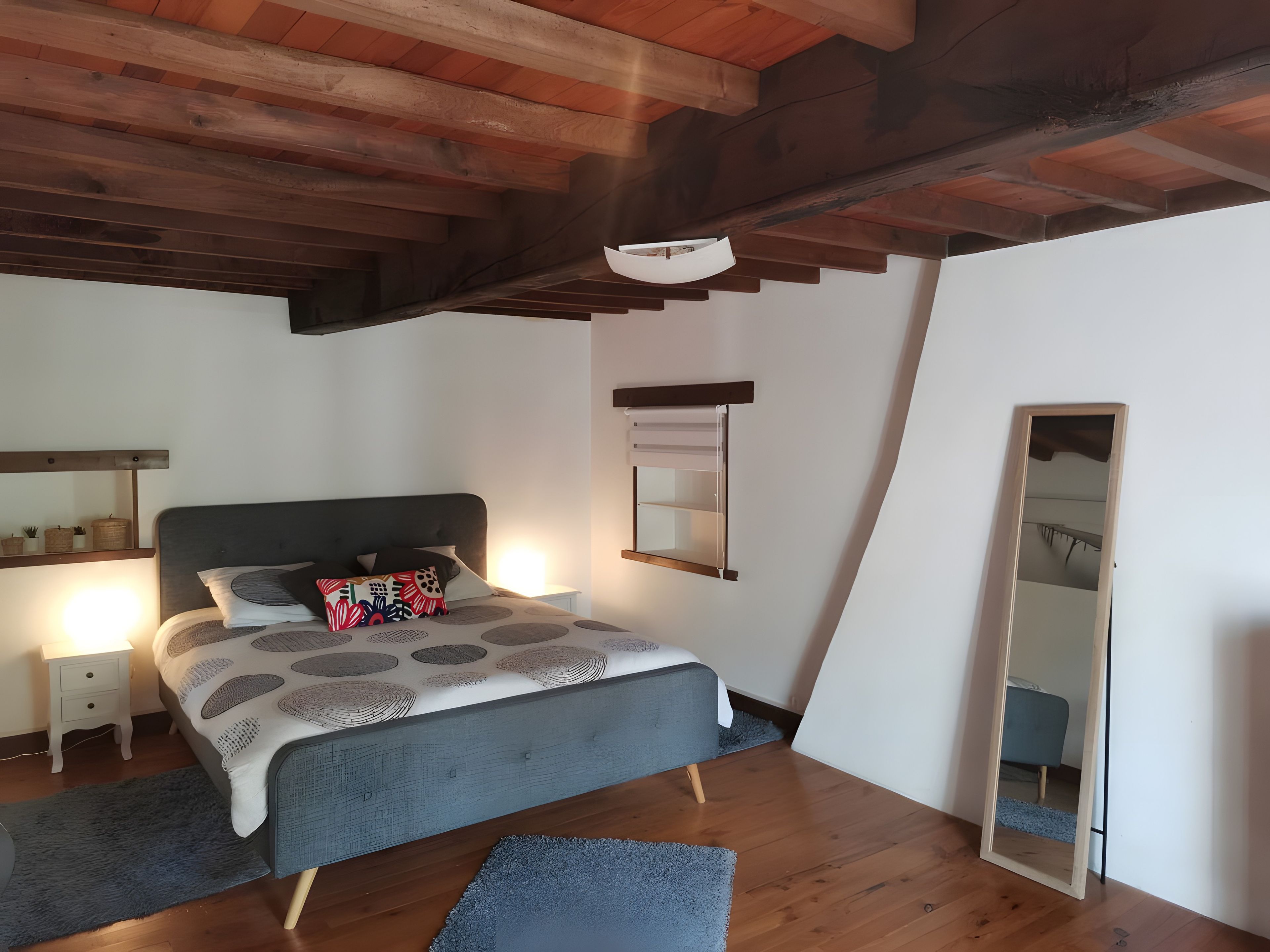 Une chambre à coucher avec un lit, des tables de chevet, un miroir et un plafond en bois.