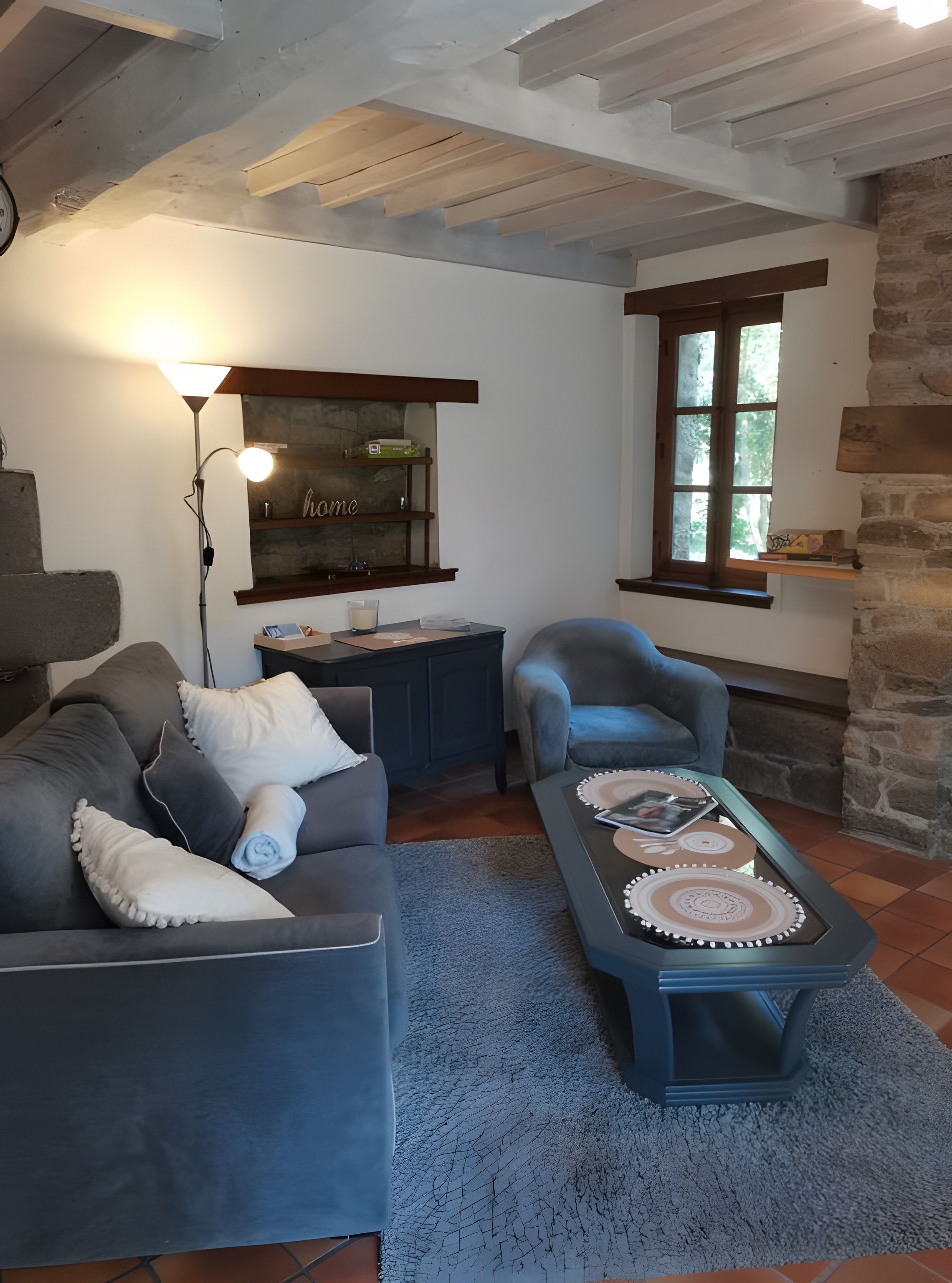Un salon chaleureux avec un canapé, un fauteuil et une table basse, une lampe et une fenêtre donnant sur un beau paysage.