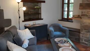 Un salon chaleureux avec un canapé, un fauteuil et une table basse, une lampe et une fenêtre donnant sur un beau paysage.
