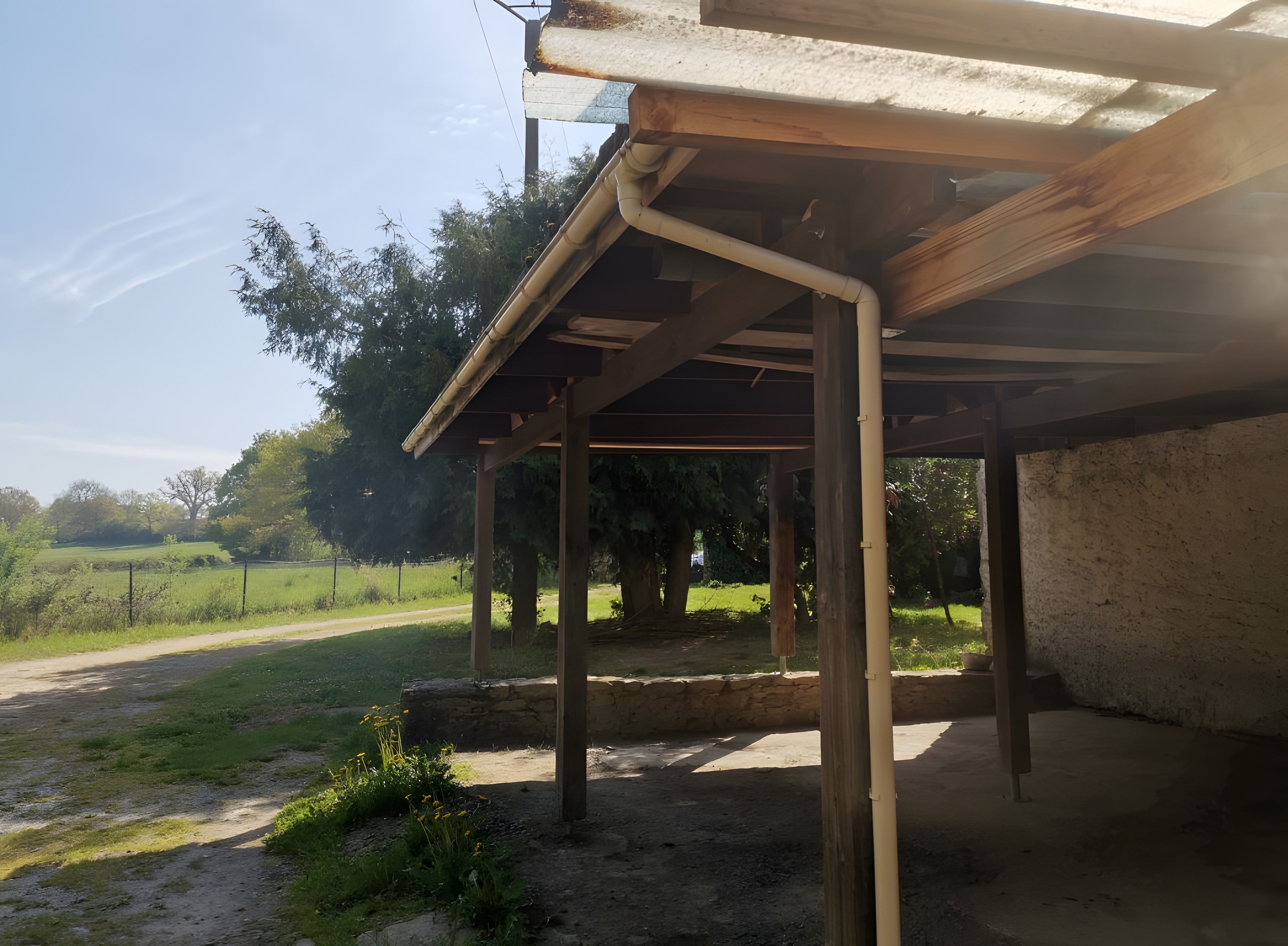 Un espace extérieur abrité, doté d’un sol en terre battue, de poutres en bois et d’un mur en pierre.