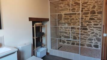 Une salle de bain avec une douche à l’italienne en pierre, des toilettes et une étagère intégrée.