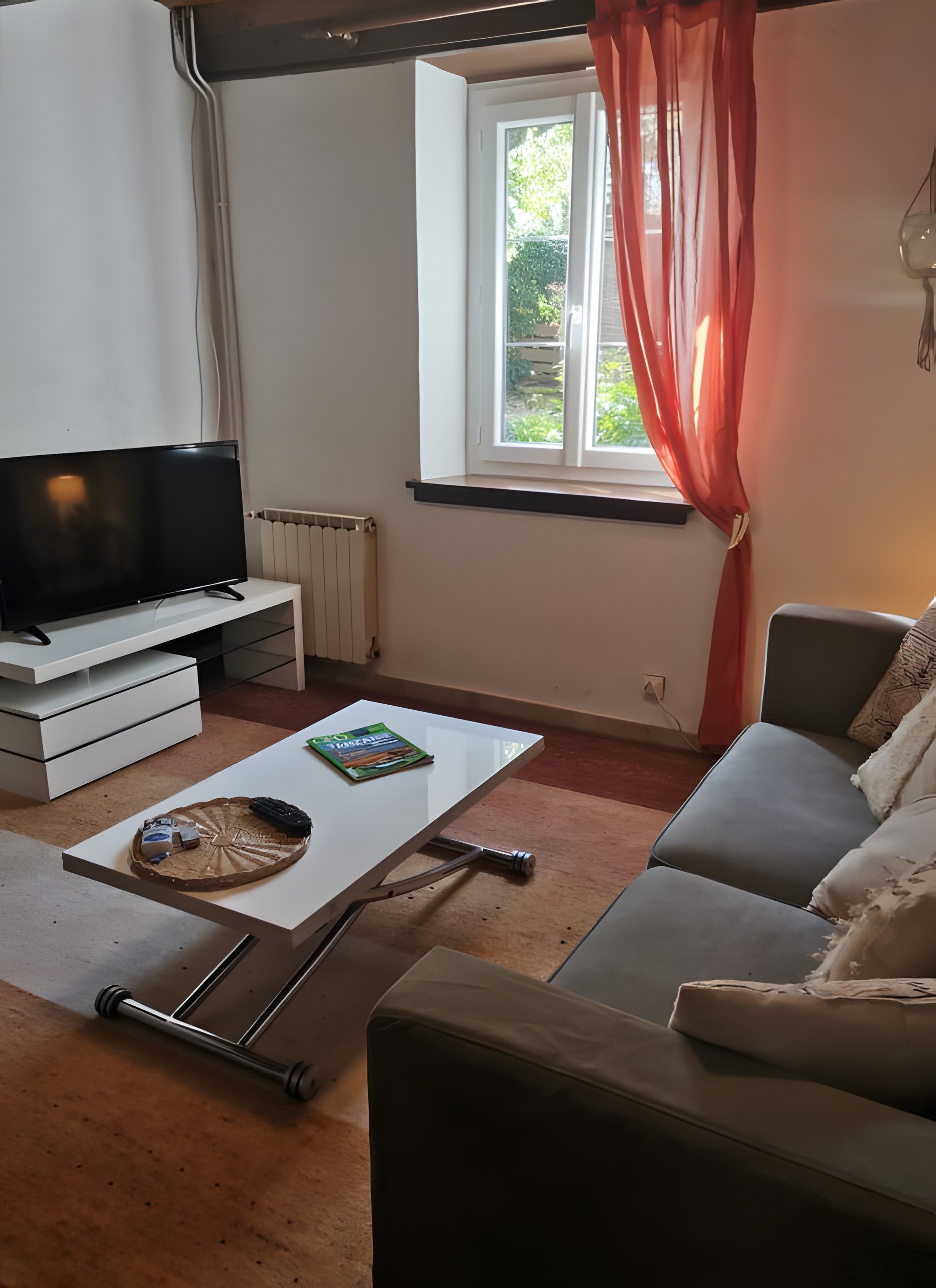 A living room with a television, a coffee table with a magazine, a sofa, and a window with curtains.