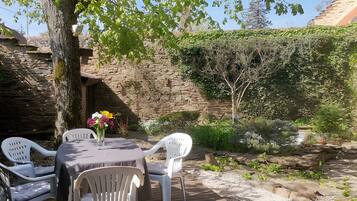A wooden deck with a table and chairs, surrounded by greenery and a stone wall.