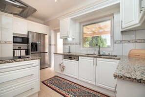 A modern kitchen with white cabinets, stainless steel appliances, a granite countertop, and a patterned rug. - Casa Oásis - 3 Bedroom Villa With Heatead Pool In Carvoeiro (Carvoeiro)