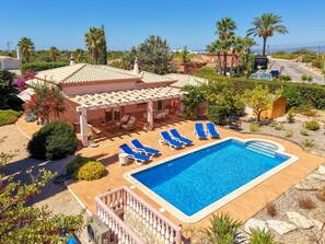 A poolside area with lounge chairs, a covered seating area, and a view of the surrounding landscape. - Casa Oásis - 3 Bedroom Villa With Heatead Pool In Carvoeiro (Carvoeiro)