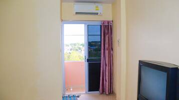A room with a television, an air conditioning unit, a sliding glass door leading to an outdoor area, and a tiled floor.