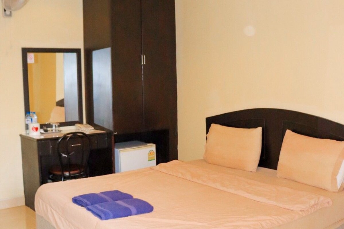 A hotel room with a bed, a desk, a chair, a wardrobe, and a mirror.