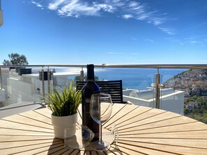 A table with a bottle and glasses on a balcony overlooking a coastal view. - Apartment in Malaga With Sea Views & Pool (Nerja)