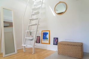 Ein Zimmer mit einer weißen Leiter, einem runden Spiegel und einem gerahmten Bild an der Wand.