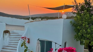 A white building with a staircase, a small table, and a chair under a sunshade.
