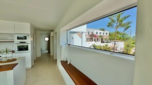 Eine moderne Küche mit eingebauten Geräten, einer hölzernen Sitzbank und Blick auf eine Wohngegend durch ein großes Fenster.