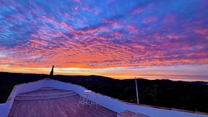 Eine Terrasse mit Blick auf einen Sonnenuntergang über einer Berglandschaft.