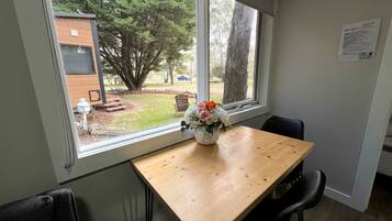 A room with a wooden table, a chair, and a window with a view of a tree and a building outside.