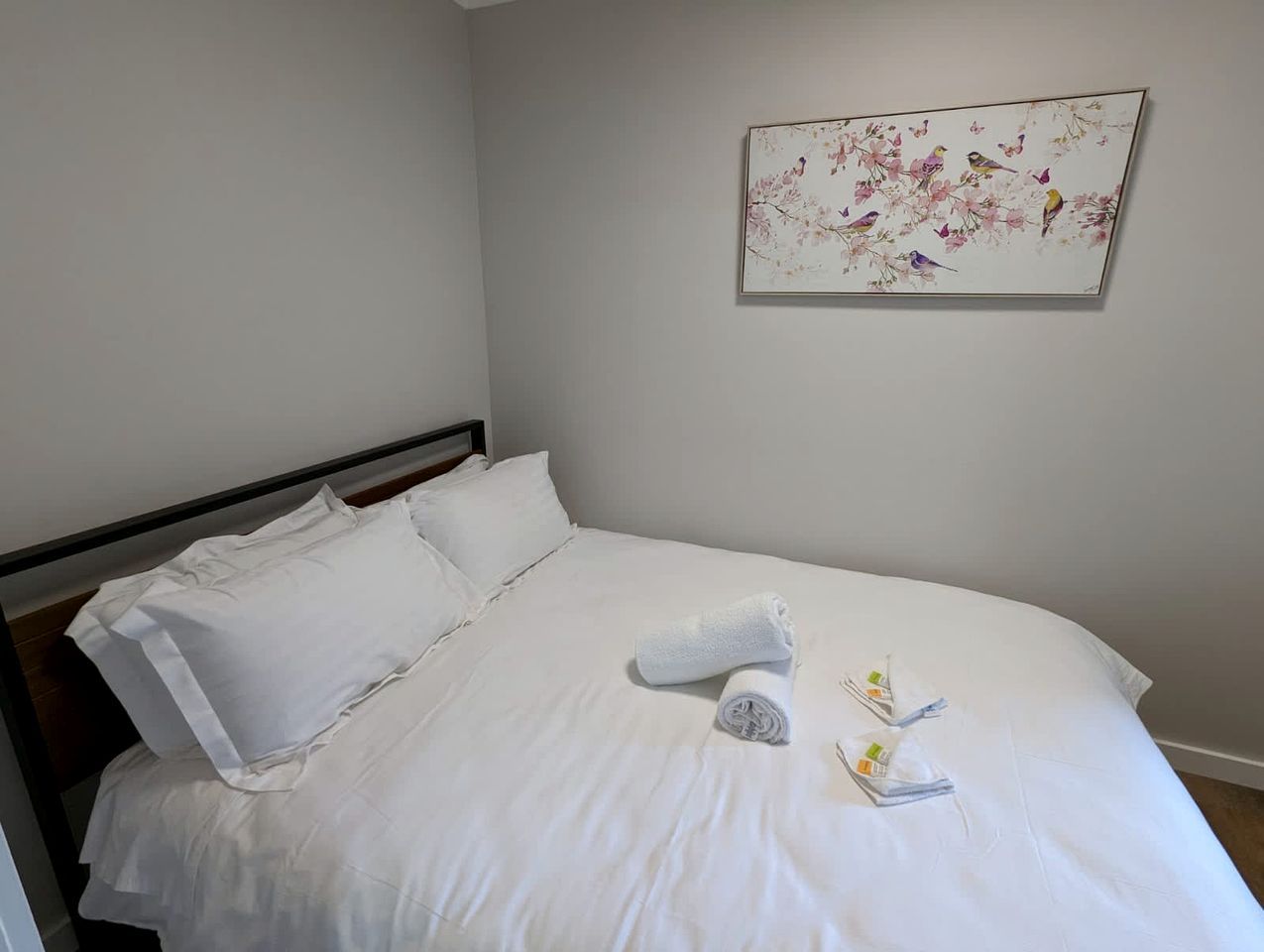 A neatly made bed with white linens, a rolled towel, and a small tray with a fork and spoon.