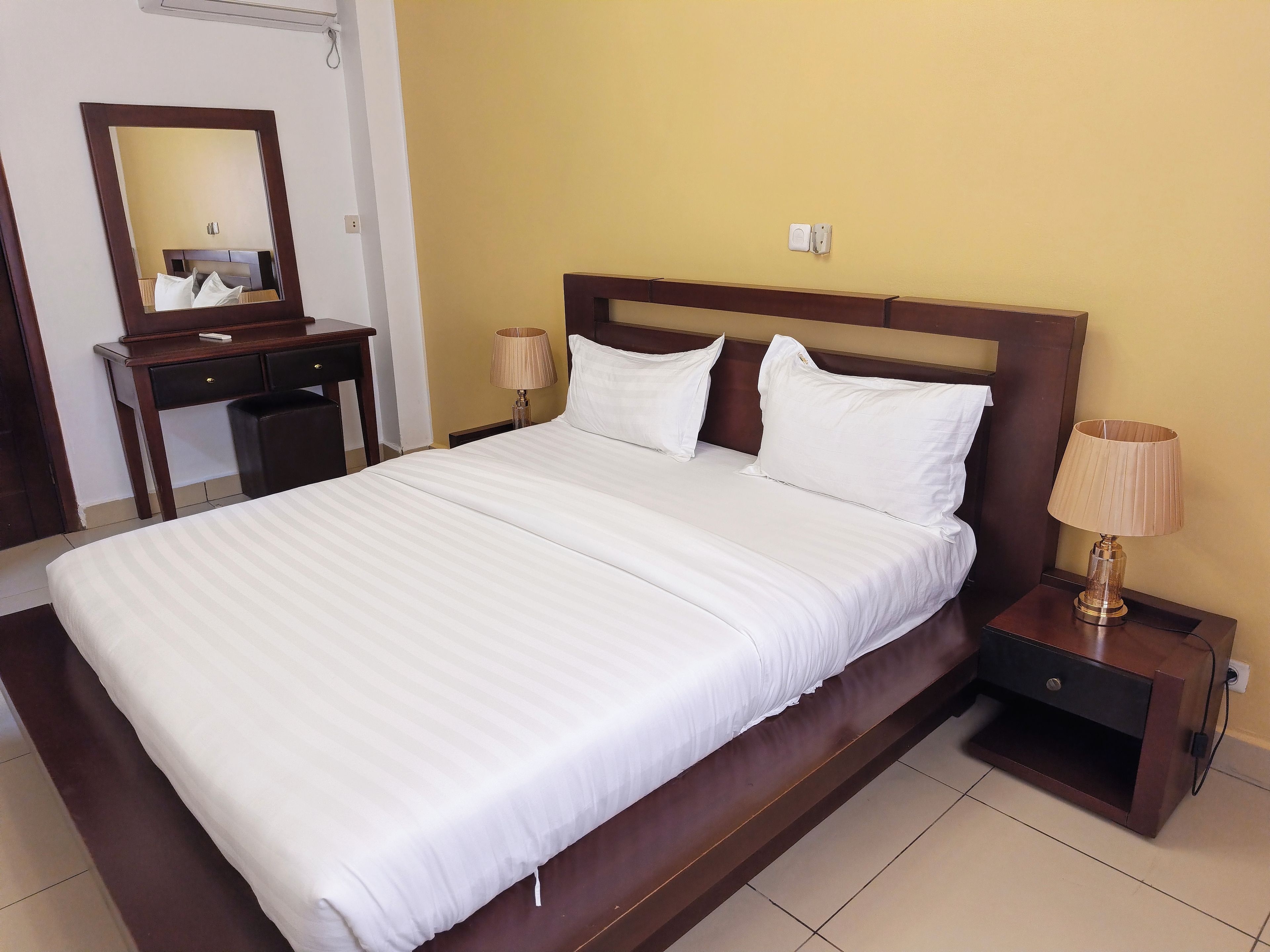A neatly made bed with white linens, a wooden headboard, and two bedside lamps.