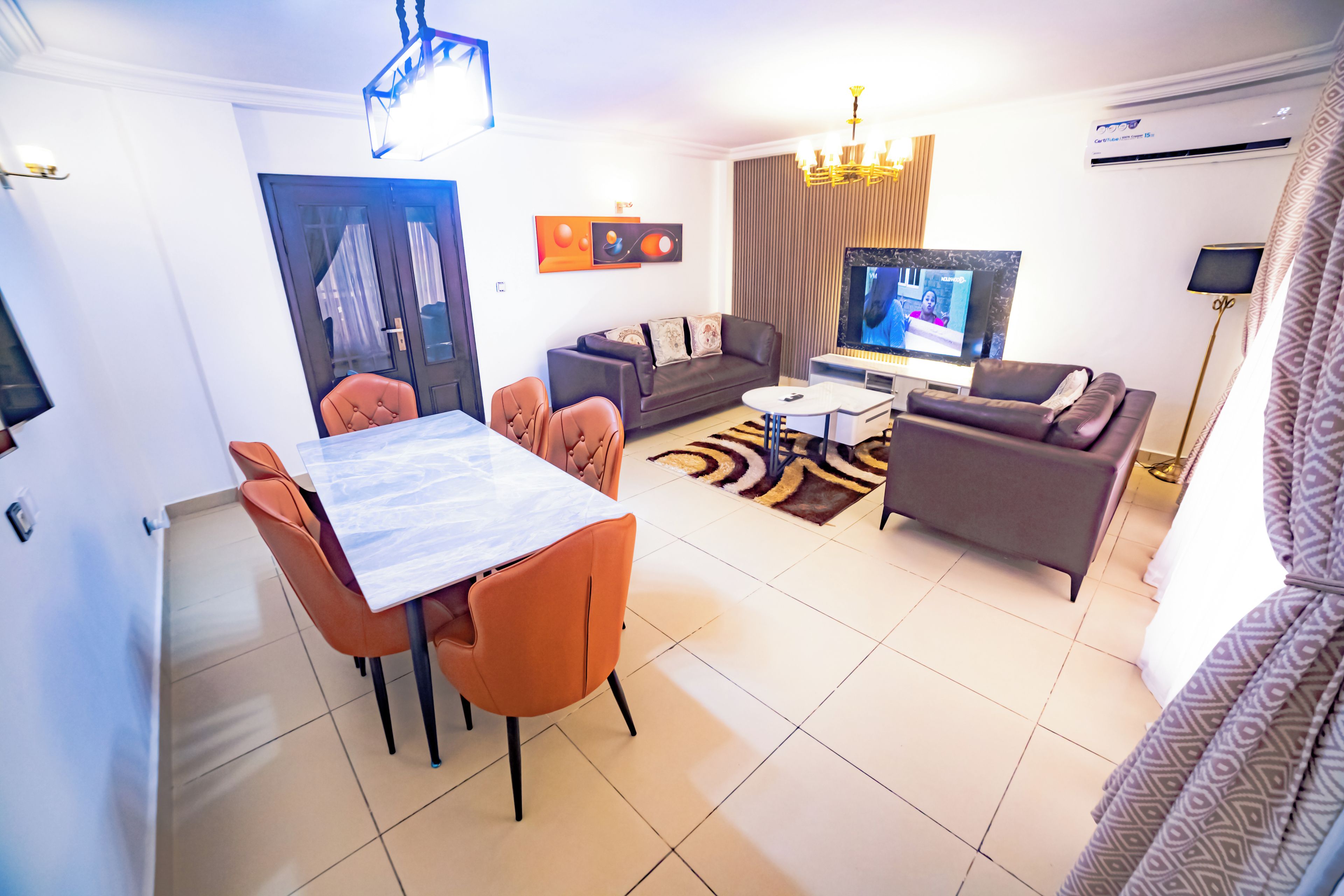 Una sala de estar moderna con comedor, un sofá, un televisor y una araña.