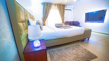 Een moderne slaapkamer met een groot bed, een nachtkastje met een lamp, een aan de muur bevestigde televisie en een raam met gordijnen.