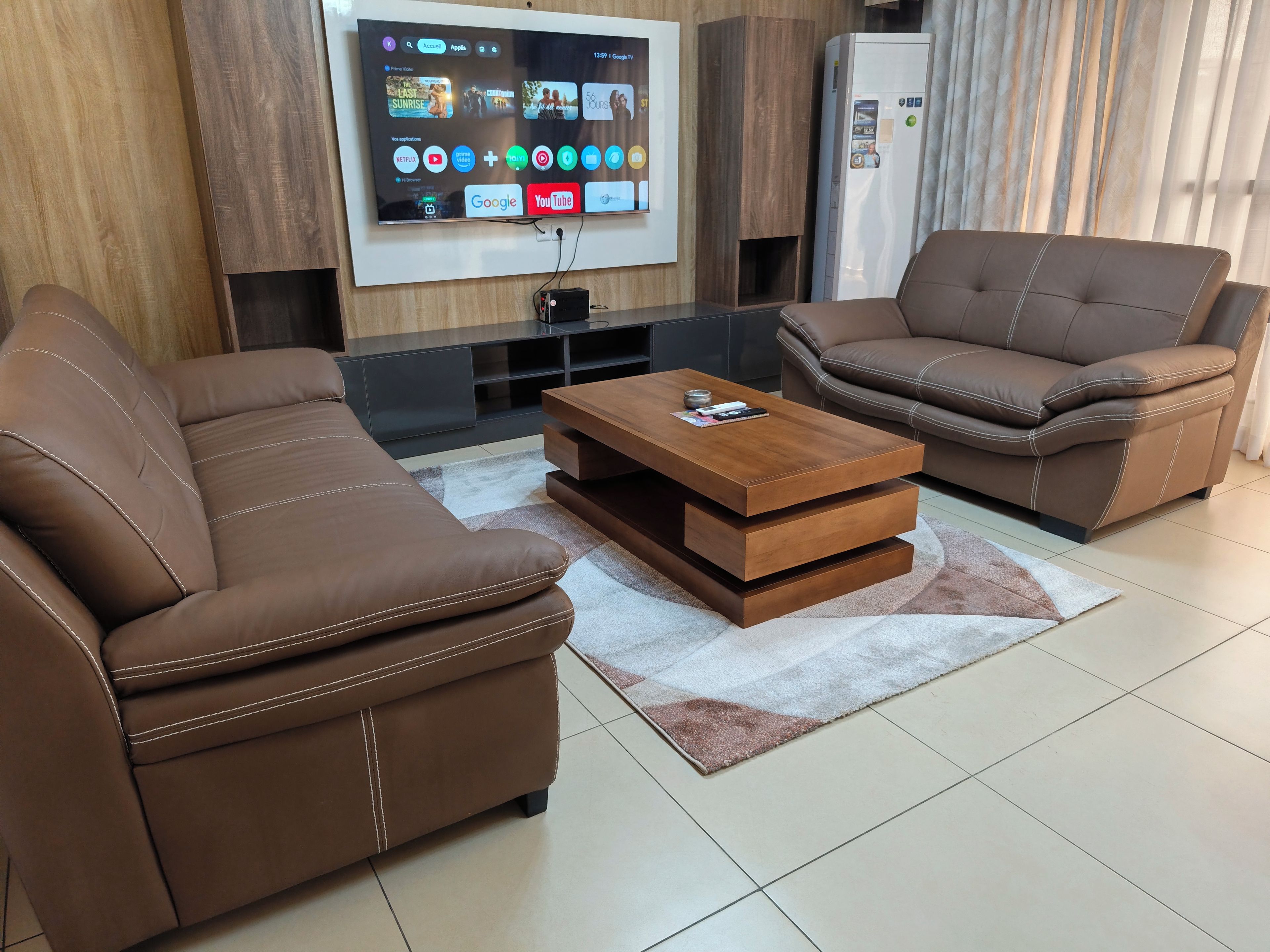 A modern living room with two brown leather sofas, a wooden coffee table, and a flat-screen TV mounted on the wall.