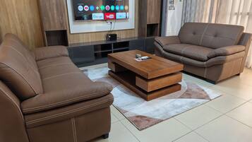 A modern living room with two brown leather sofas, a wooden coffee table, and a flat-screen TV mounted on the wall.