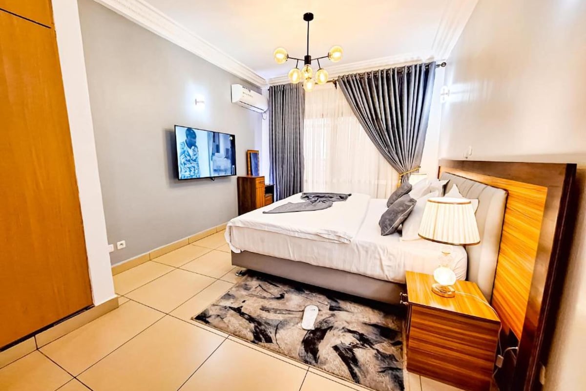 A modern bedroom with a bed, bedside tables, a TV, and a chandelier.