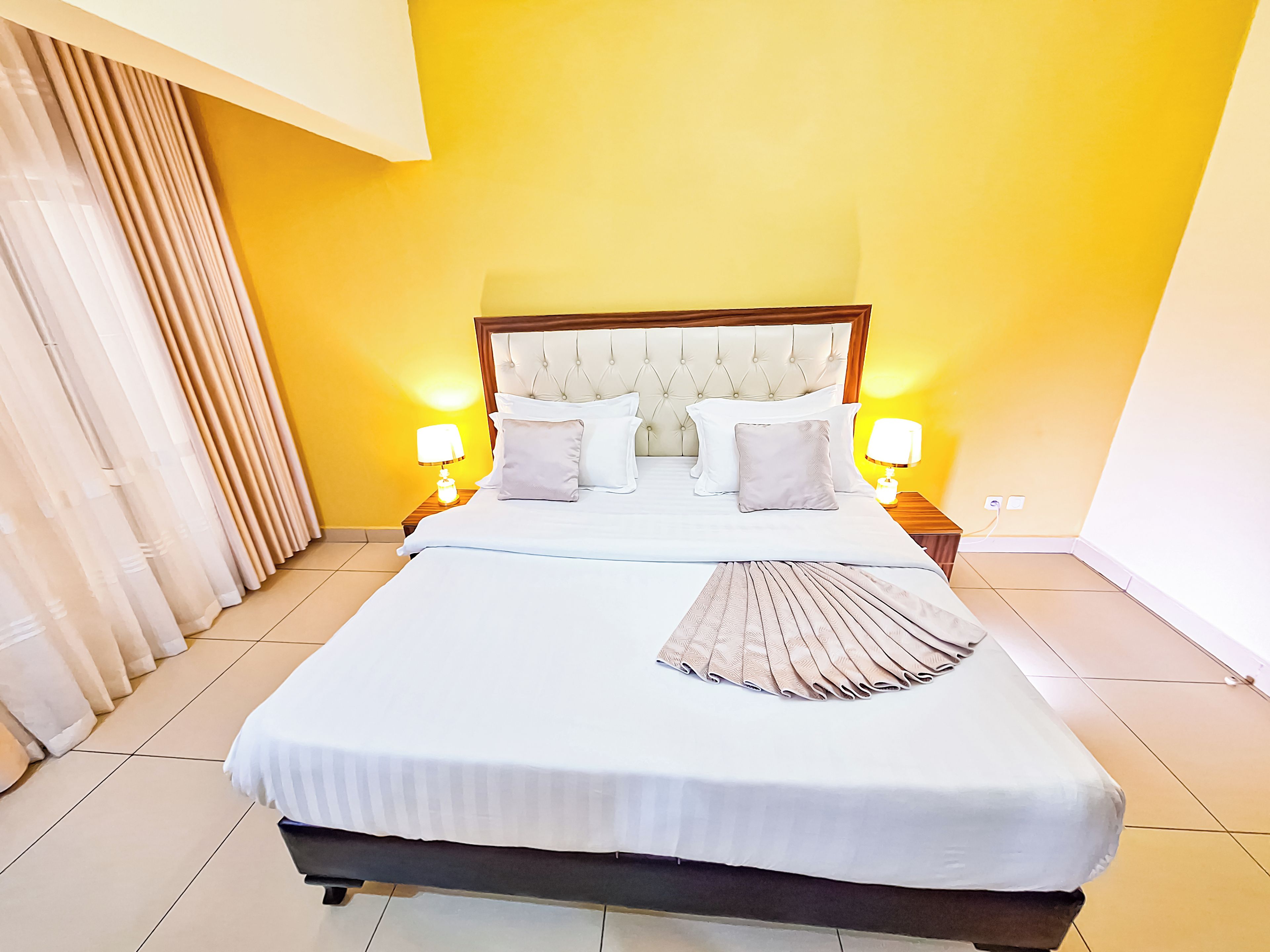 Una habitación de hotel con una cama grande, dos mesitas de noche y un cabecero.