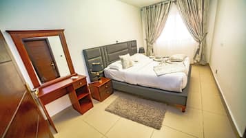 Een slaapkamer met een bed, nachtkastje, dressoir, spiegel en een raam met gordijnen.