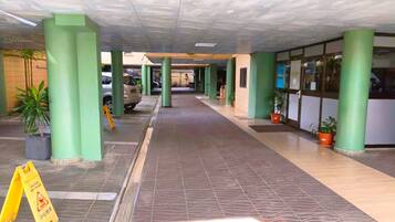 A covered walkway with green pillars, tiled flooring, and potted plants.