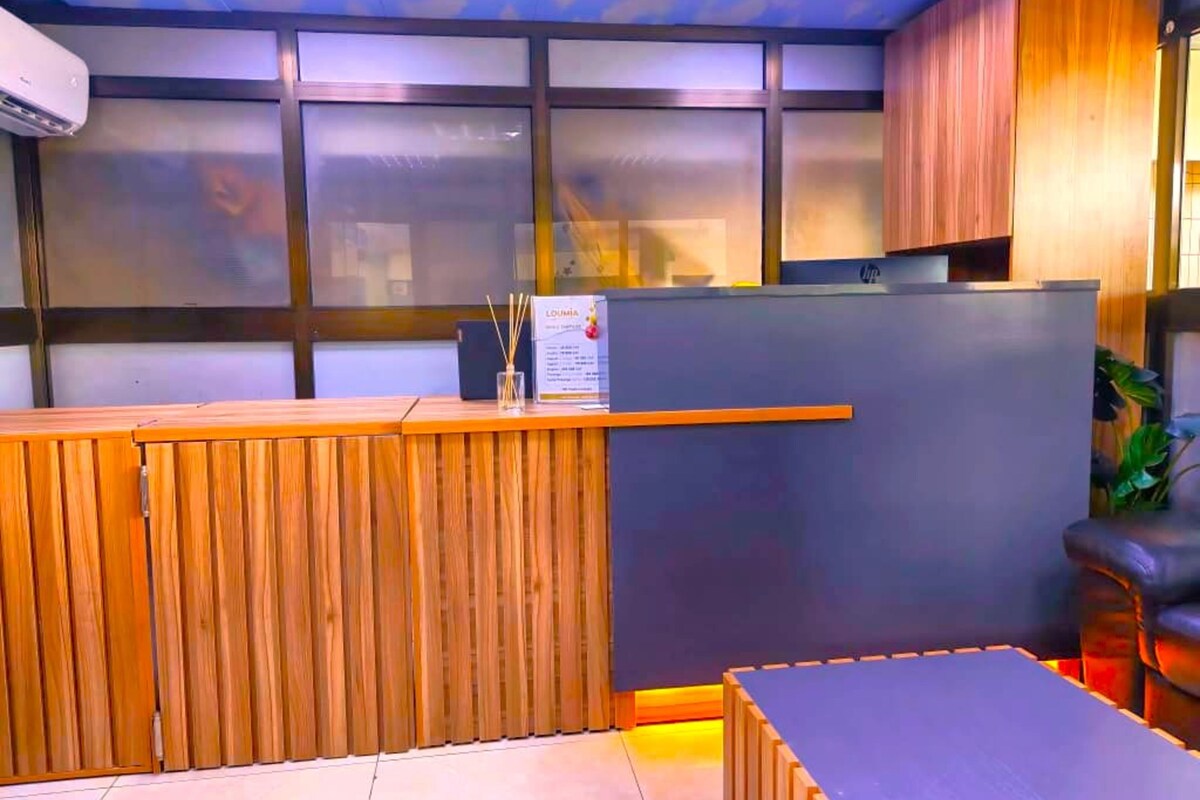 A reception area with a wooden reception desk, a grey wall, and a plant in the corner.