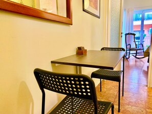 A dining area with a table and chairs, a wooden frame on the wall, and a door leading to an outdoor area. - Athens Home (Athina)