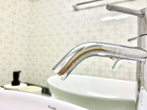 A bathroom with a modern faucet, a white sink, and a tiled wall. - Athens Home (Athina)