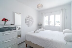 A white bedroom with a bed, a dresser, a mirror, a wall decoration, and a window with curtains. - Apartment in Nerja Near Burriana Beach (Nerja)