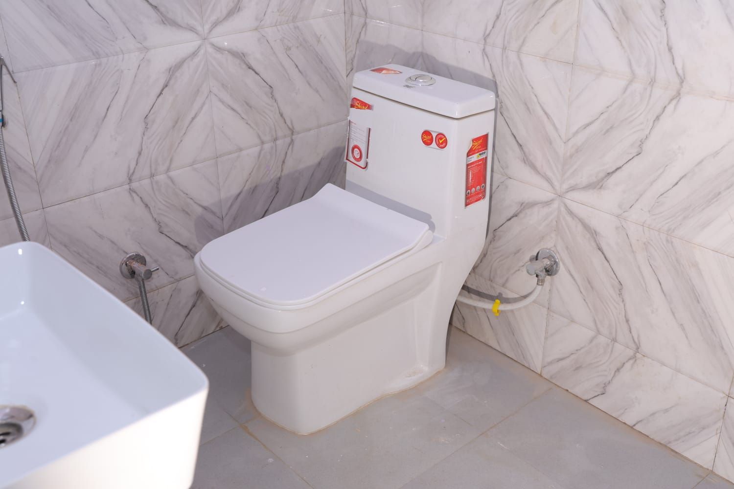 Un baño con inodoro y lavamanos blancos, y paredes con diseño de mármol.
