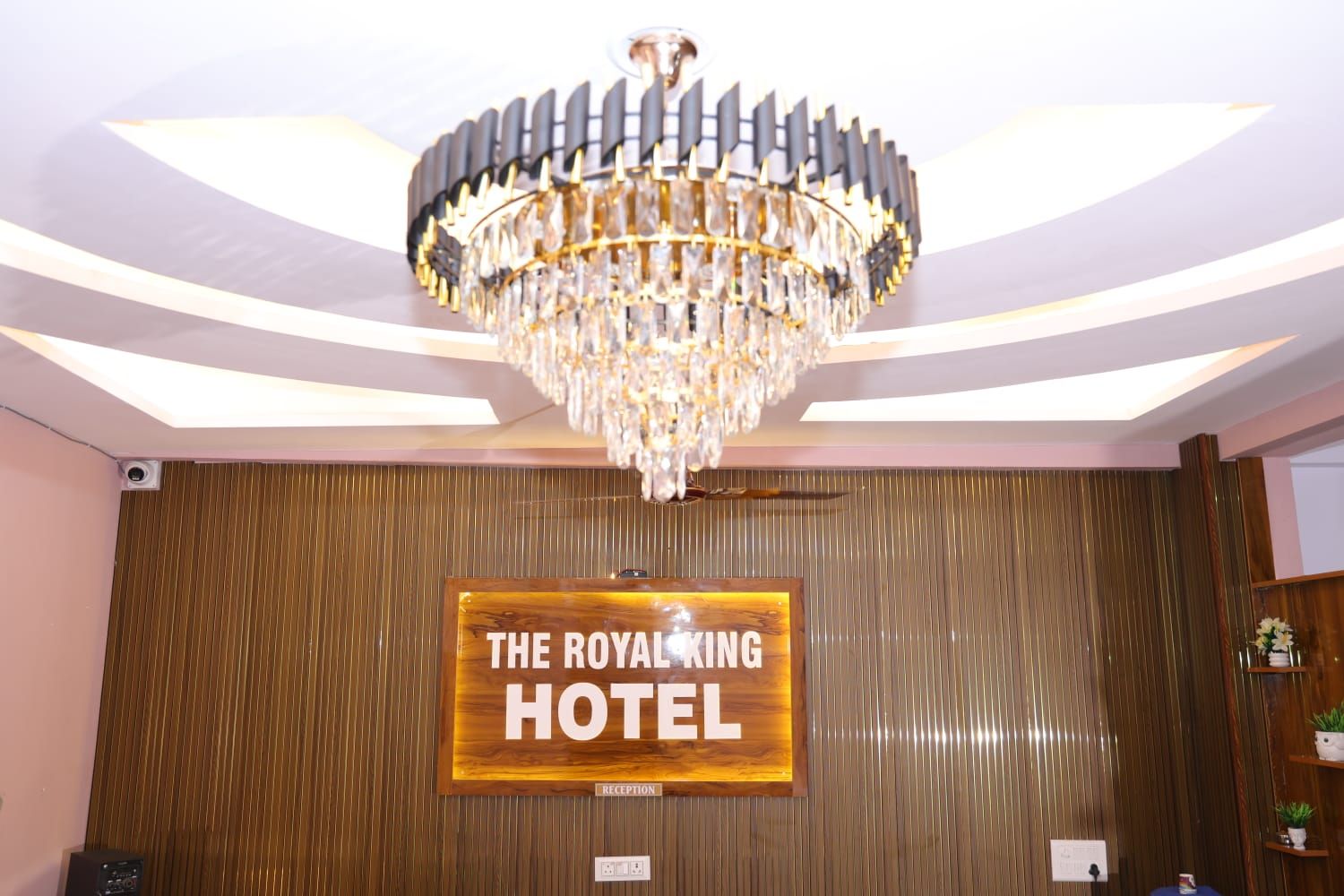 A reception area with a chandelier, a wooden reception desk, and a sign that reads 'THE ROYAL KING HOTEL.'
