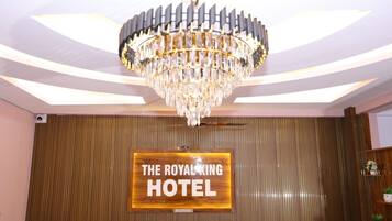 A reception area with a chandelier, a wooden reception desk, and a sign that reads 'THE ROYAL KING HOTEL.'