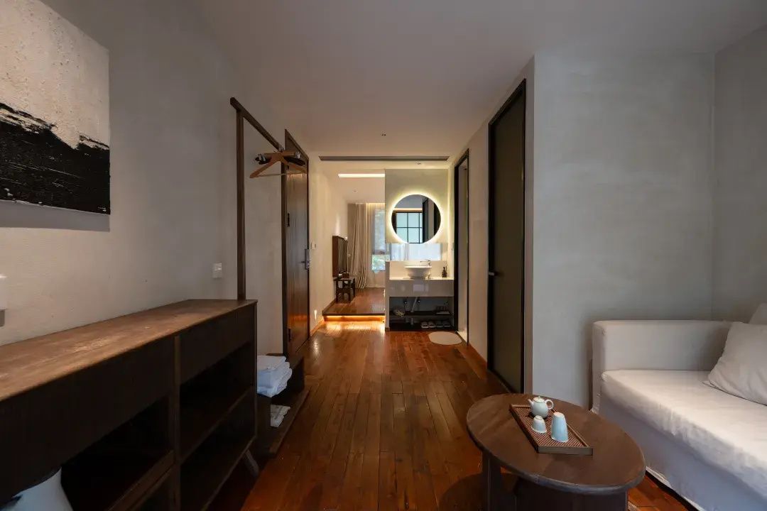 Un pasillo que conduce a un baño con un banco de madera, un espejo redondo y un sofá blanco.