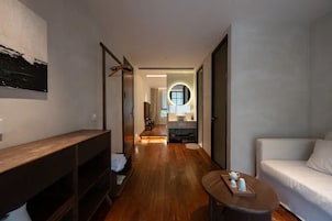 Un pasillo que conduce a un baño con un banco de madera, un espejo redondo y un sofá blanco.