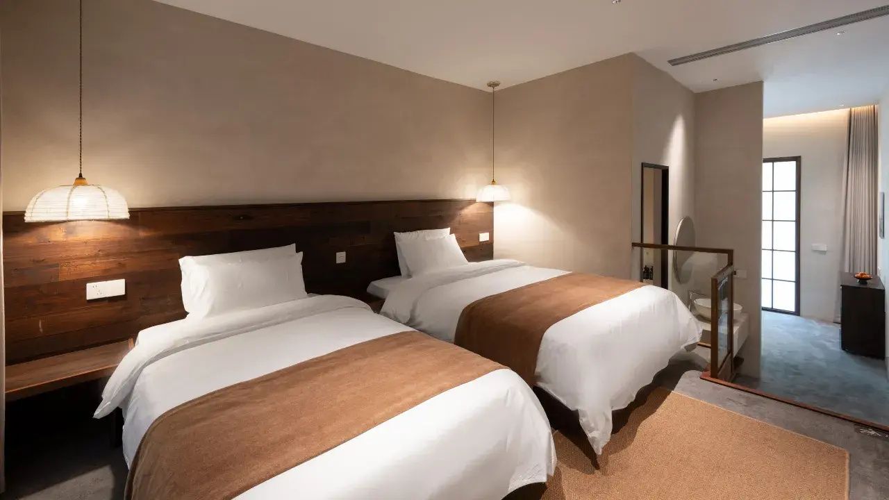 Une chambre d’hôtel avec deux lits, une tête de lit en bois, un miroir et une vue sur l’extérieur.