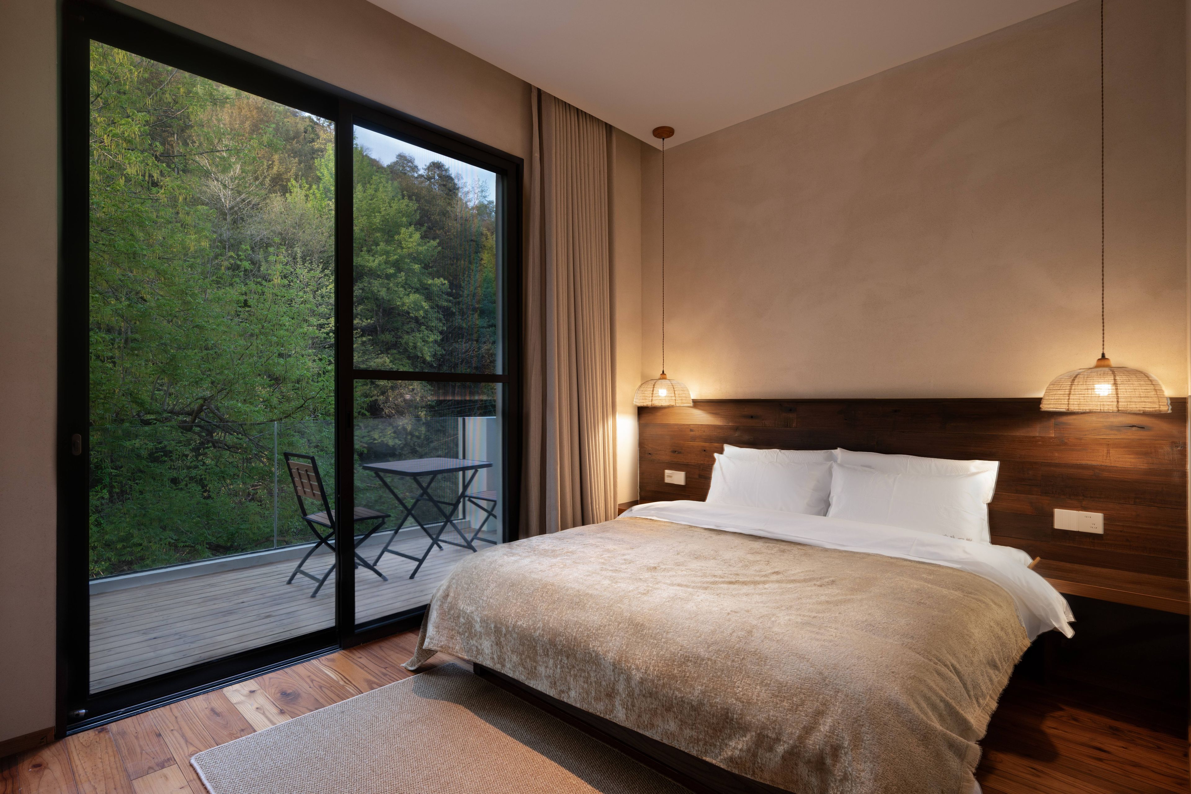 A bedroom with a large sliding glass door, a bed with white linens, a wooden headboard, and a hanging light fixture.