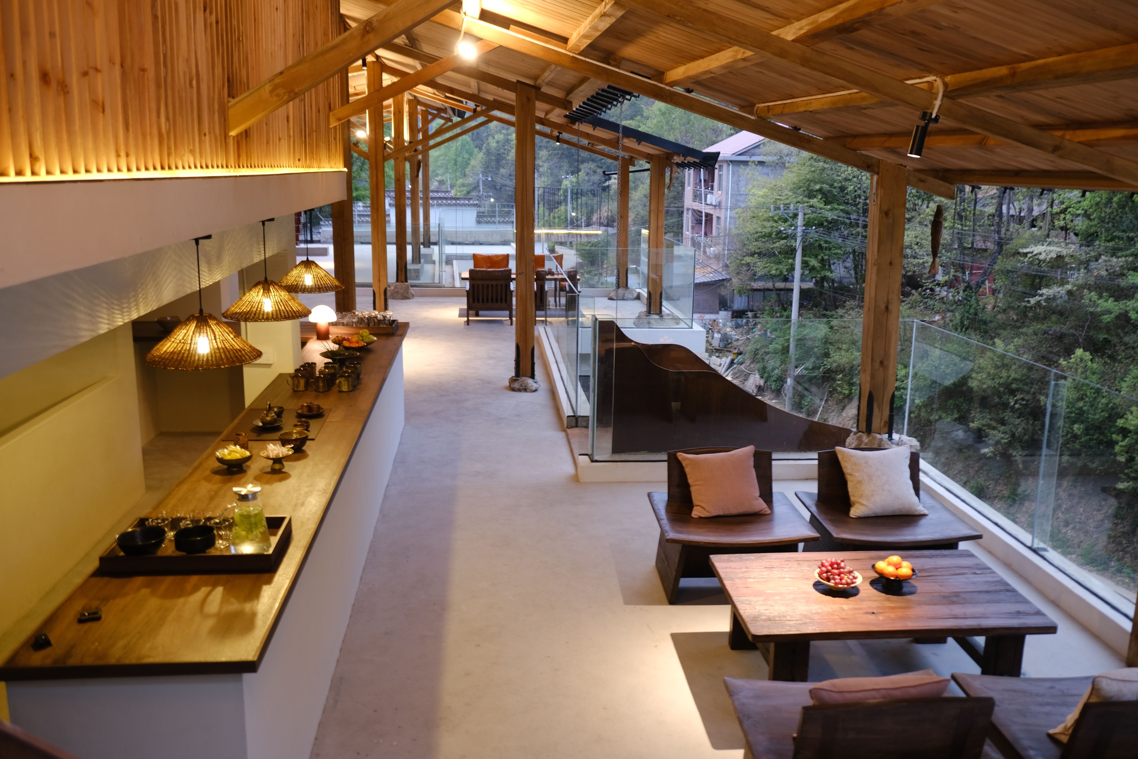 Um interior moderno com uma longa mesa de jantar, área de estar e grandes janelas com vista para o exterior.